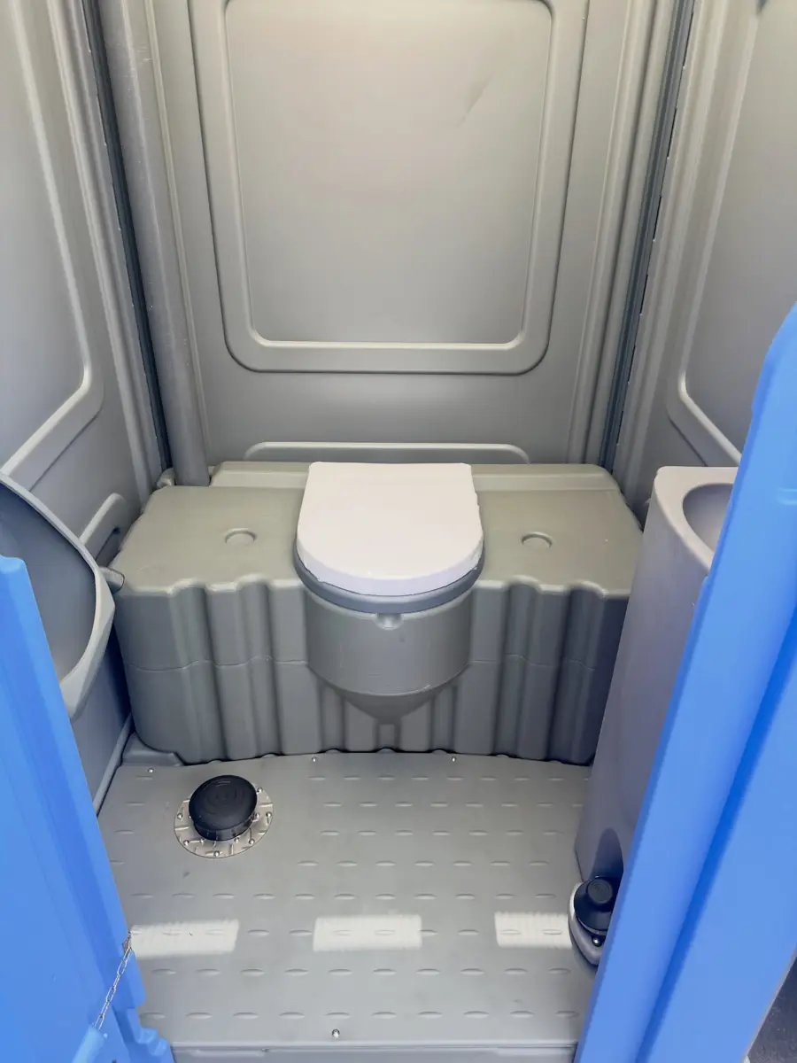 Inside a standard porta potty showing the toilet seat, molded floor and side wall