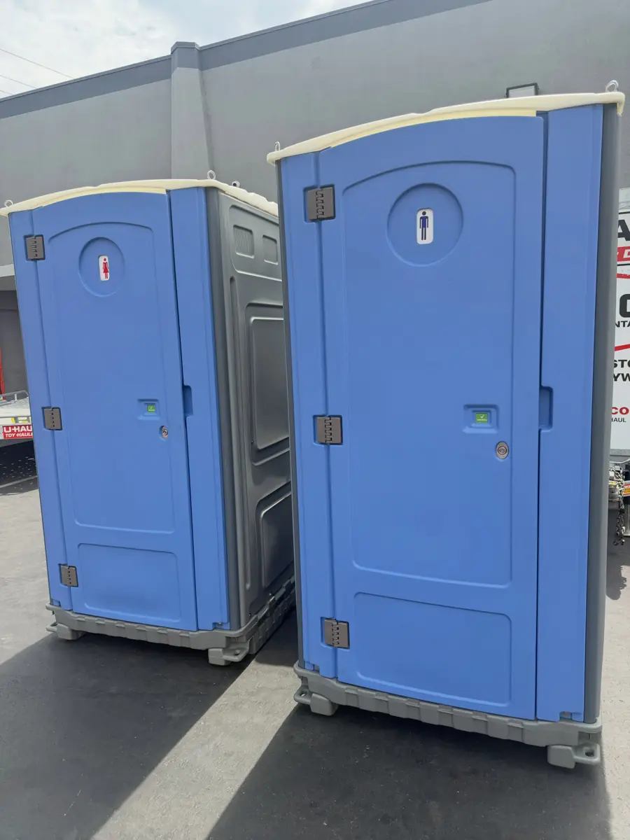 Two blue standard porta potties in a driveway